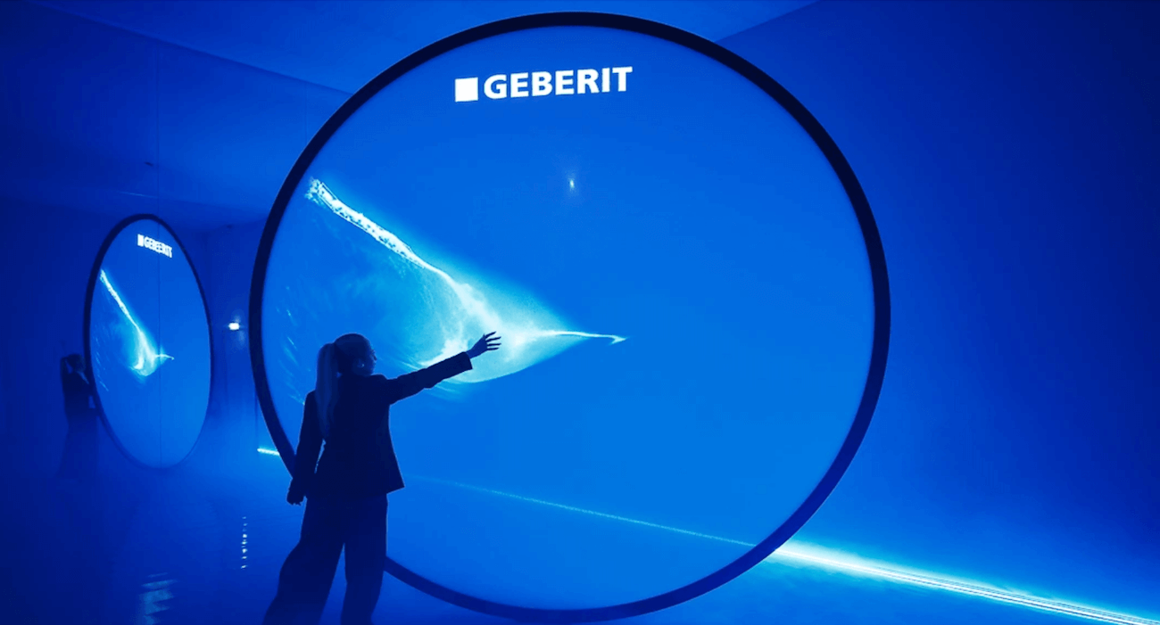 Una persona interagisce con un’installazione artistica di grandi cerchi luminosi blu firmata Geberit, che evocano la forma e il movimento dell’acqua. L’atmosfera è futuristica e suggestiva.